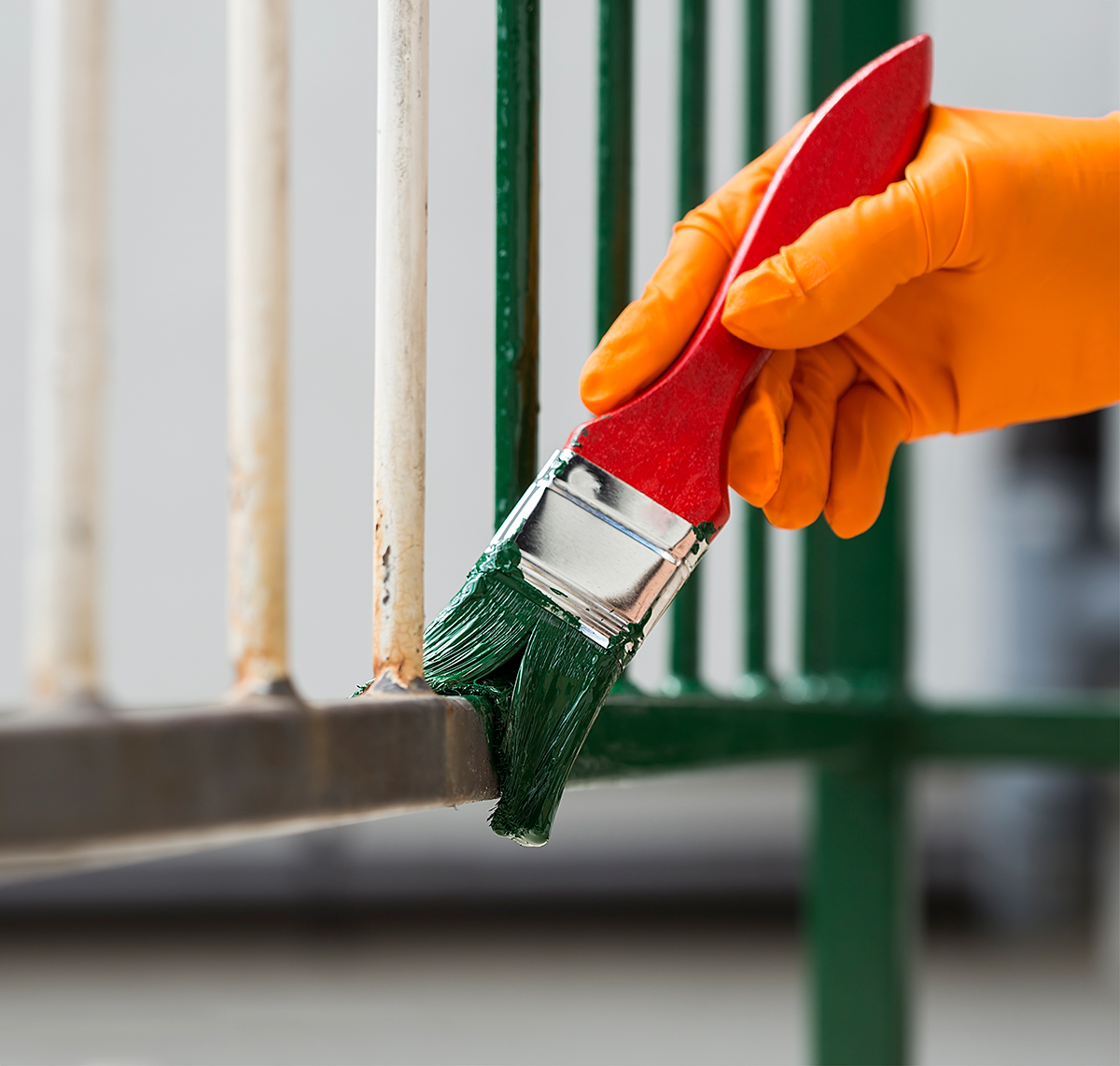 A gloved hand holding a paint brush dipped in green paint, painting a metal railing